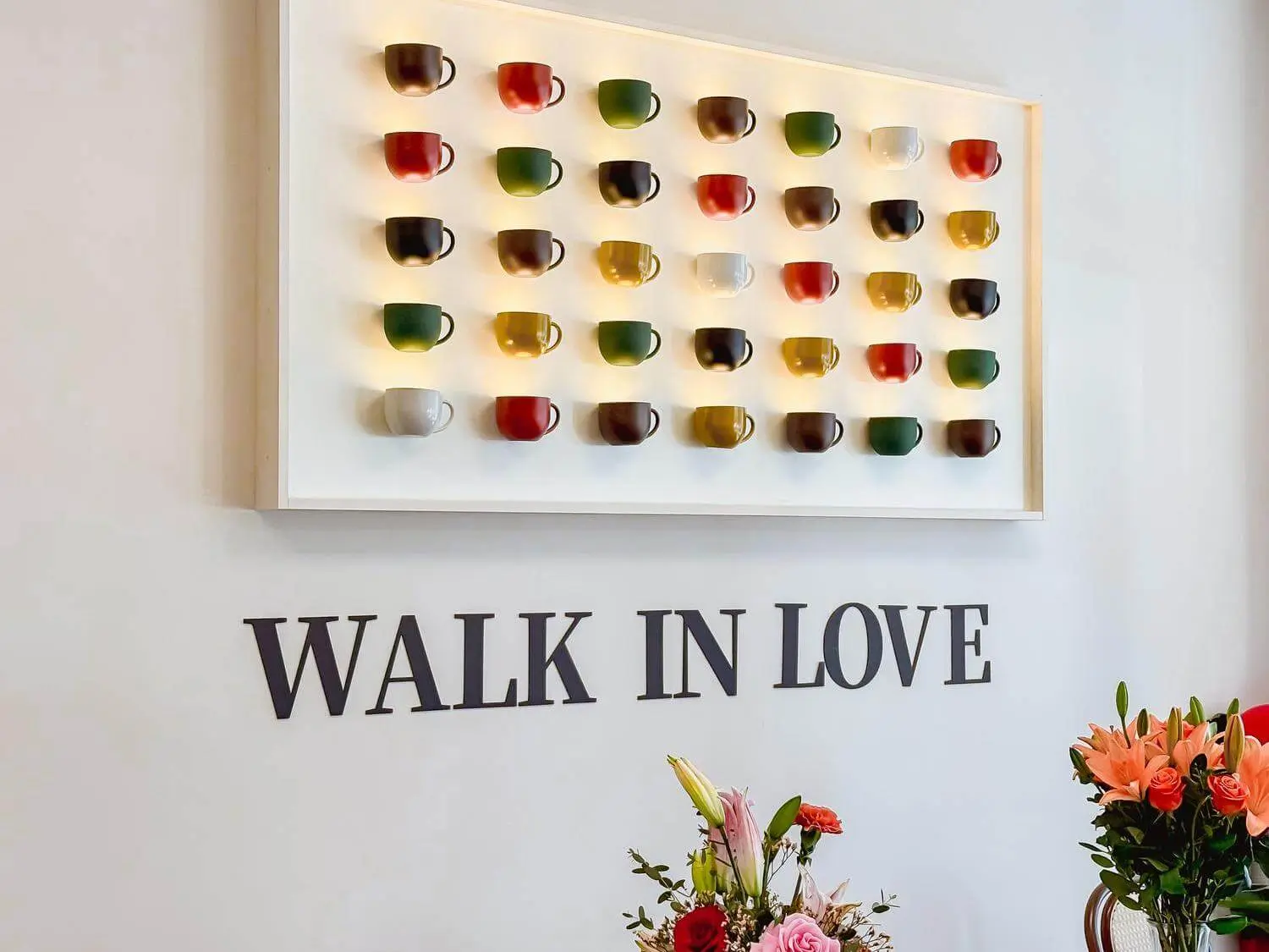 Wall decor with colorful cups and "WALK IN LOVE" sign at Bliss Café, a Coffee Shop in Oviedo